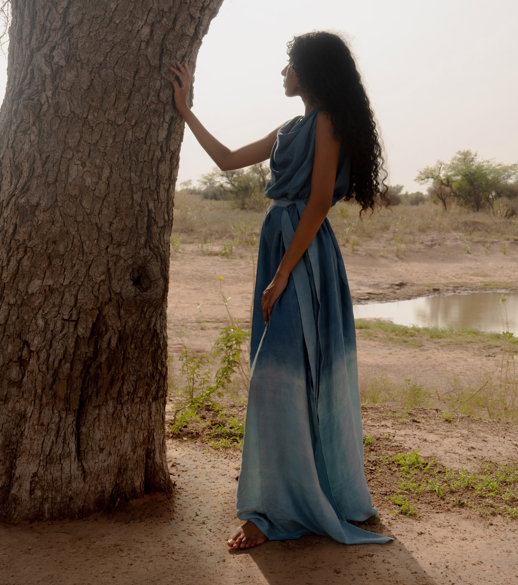 Hera dress in indigo blue silk beside a large tree